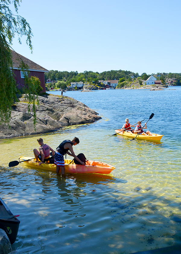 To gutter er på vei oppi en kajakk. I bakgrunnen ser vi to gutter i en annen kajakk.