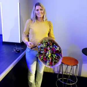 Dame i gul genser med blomster og vinnertrofé i hendene.