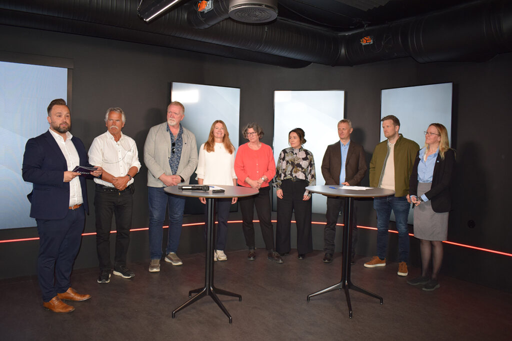 Ni kvinner og menn poserer foran kamera i en halvsirkel