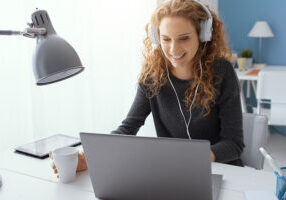 Happy young student girl wearing headphones and watching movies online, leisure and entertainment concept